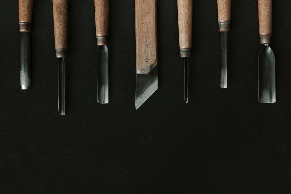 A variety of wood carving tools neatly arranged on a dark fabric background, showcasing craftsmanship.
