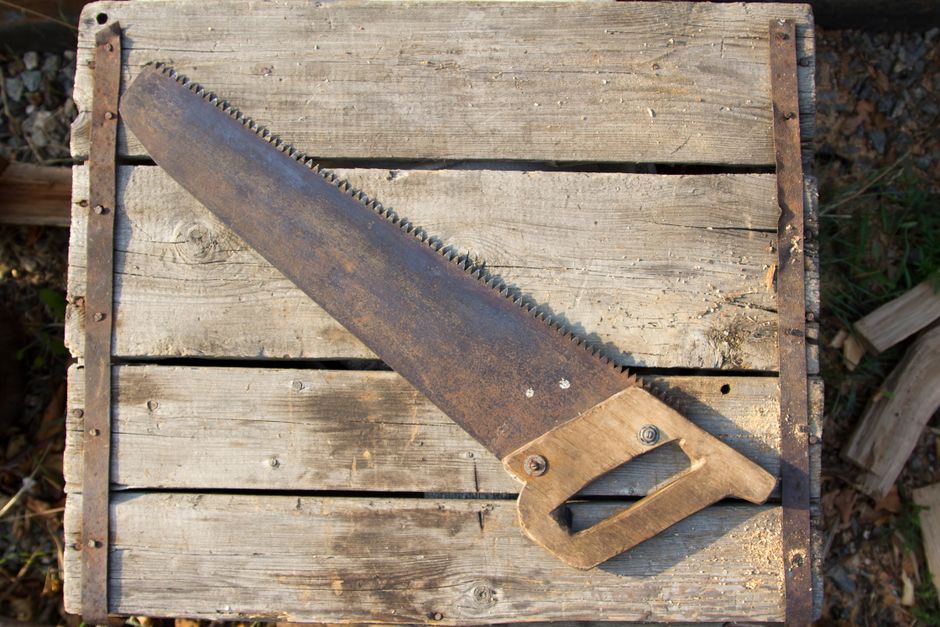 A worn vintage hand saw placed on an old wooden table outdoors. Perfect for antique tool themes.