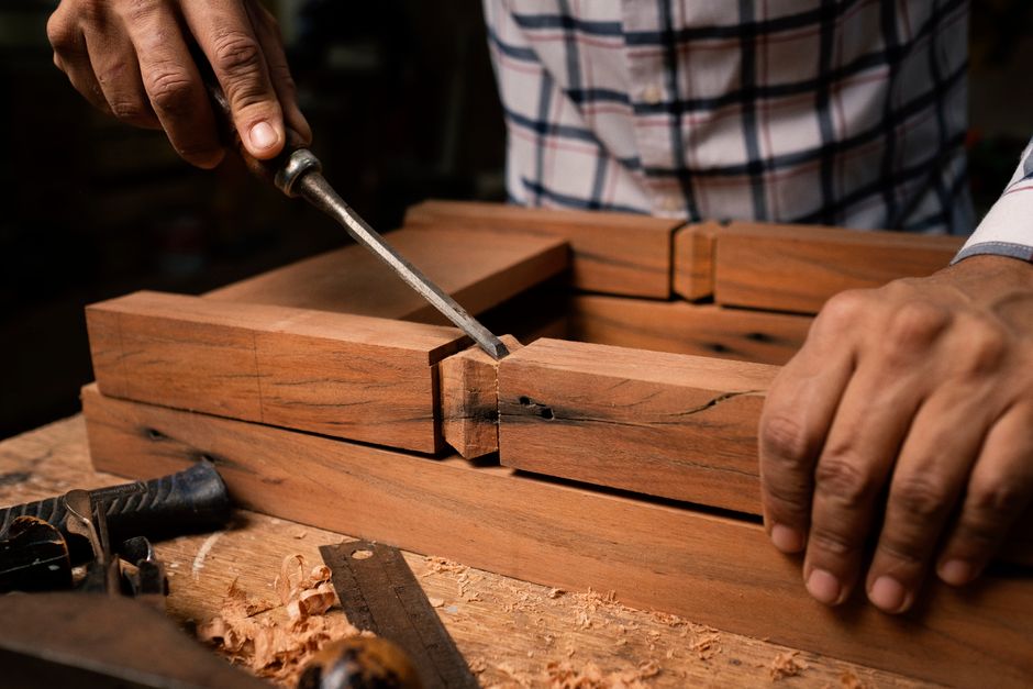 Focused view of a person skillfully using a chisel on wooden pieces indoors.