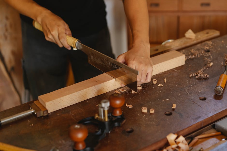 From above of crop anonymous male carpenter sawing lumber plank placed on workbench in joinery