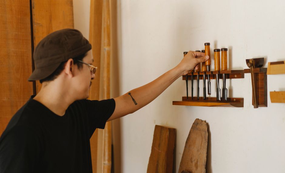 Side view of adult male taking chisel from professional set on wall working in own woodwork studio